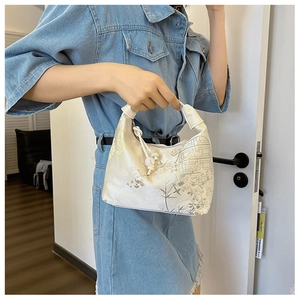 Detail of a beige satin handbag with floral embroidery and elegant beaded tassel accents