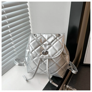 Detailed close-up of metallic silver quilted mini backpack with chain strap on white windowsill