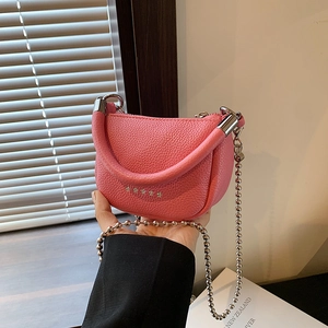 Mini pink lychee leather saddle bag with silver ball chain shown in a home setting