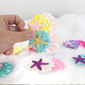 Detailed view of colorful sequin shell and starfish hair clips on a white plush rug