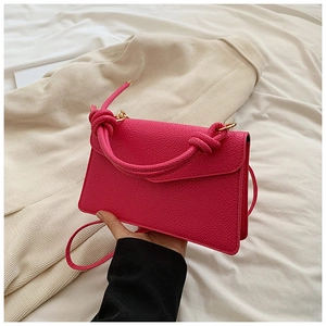 Close-up of hot pink lychee grain leather bag featuring a chunky knot handle and gold hardware