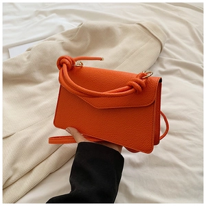 Macro shot of orange lychee grain leather small bag with knotted handle and envelope flap
