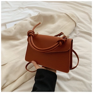 Detail of a brown lychee pattern leather bag with unique knotted handles on white fabric