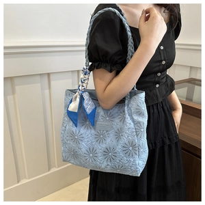 Close-up of light blue quilted tote bag with floral embroidery and woven strap details