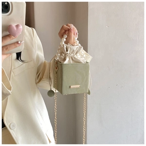 Detail of light green square bucket bag with pearl handle and golden chain strap