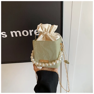 Detail of light green bucket bag with pearl handle and golden chain shoulder strap