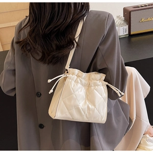 Detailed side view of off-white quilted bucket bag with drawstring and thin leather strap