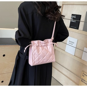 Detail of pink quilted drawstring crossbody bag with adjustable strap on a model