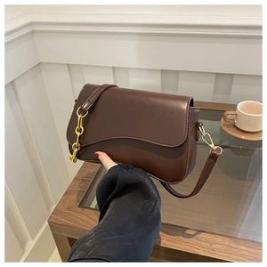Detail of wave-edged brown leather flap and polished gold metal rings on shoulder strap