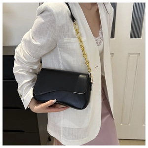 Close-up of wavy cut flap and gold chunky chain strap on black leather shoulder bag
