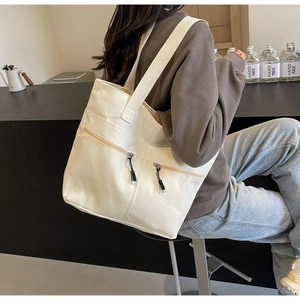 Detail of off-white canvas tote bag featuring double front zipper pockets and wide straps