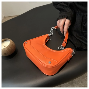 Detail of orange hobo bag with silver chain, studs and leather handle in hand