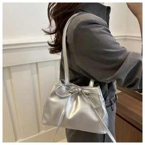 Silver metallic shoulder bag with bow drawstring detail worn by a model in gray suit