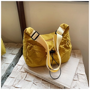 Macro shot of yellow nylon hobo tote featuring pleated texture and wide beige strap