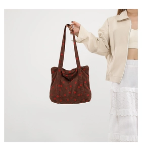 Close-up of strawberry embroidery on brown corduroy tote bag held by a model