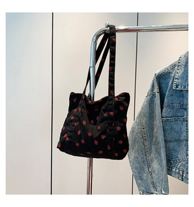 Detail of corduroy texture and red strawberry print on this black tote bag surface