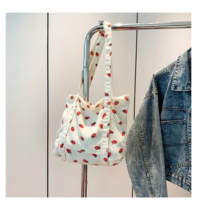 Close-up of cream corduroy tote bag featuring red strawberry patterns and side pocket