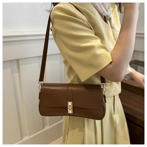 Sac baguette en cuir marron avec fermoir tournant doré porté à l'épaule du modèle