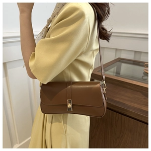 Détail d'un sac sous le bras marron foncé avec boucle dorée sur une robe jaune