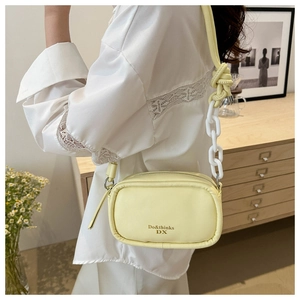 Detail view of yellow crossbody bag featuring chunky white chain and adjustable strap