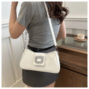 Close-up of white underarm bag with sparkling crystal buckle and chain strap detail