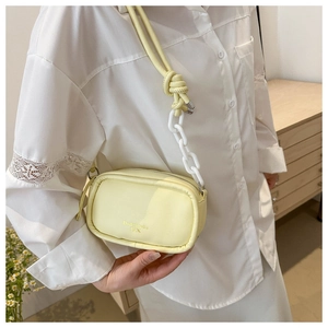 Detail of a creamy yellow PU leather camera bag with a white chunky chain and knot strap