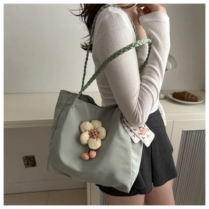 Close-up of light green tote bag featuring floral plush charm and illustrated silk scarf