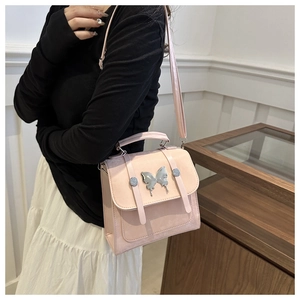 Detail of light pink PU leather crossbody bag featuring a silver butterfly pendant charm