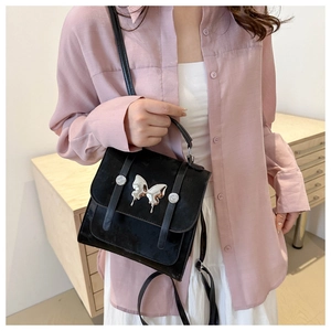 Detail of a black velvet handbag featuring a large silver butterfly buckle and straps