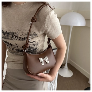 Detail of a brown leather crescent shoulder bag featuring a silver bow and knot strap