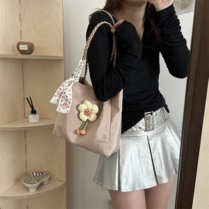 Khaki tote bag with woven handles and flower charm worn by a model in casual style