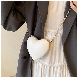 White heart-shaped hard shell crossbody bag with gold metal trim and a slim chain strap