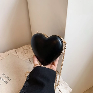 Detail of a black heart-shaped clutch bag with golden metal frame and chain strap