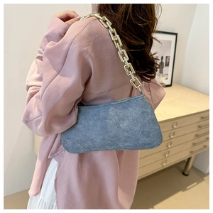 Chic grey suede underarm bag with chunky gold chain strap worn by model in a cozy room