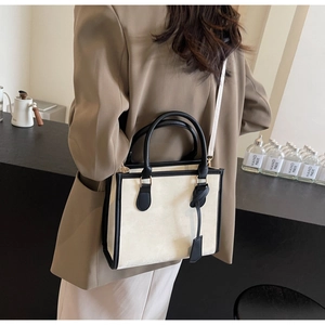 Gros plan du sac cabas crème avec poignées en cuir noir porté par un mannequin en veste