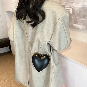 Elegant black heart-shaped crossbody bag with gold chain strap worn by a model