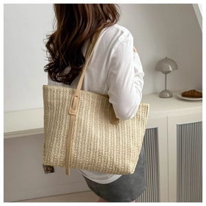 Detail of minimalist beige woven straw tote bag with slim leather straps and side ribbons