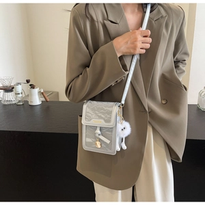 Detail of silver metallic textured crossbody phone bag with gold fashion logo and plush charm