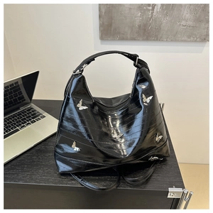 Detail of glossy black shoulder bag featuring silver butterfly metal accents and sleek finish