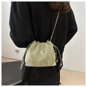 Detail view of sage green bucket bag featuring silver butterfly accents and chain strap
