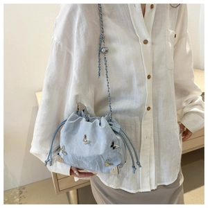 Detail of light blue drawstring bucket bag with silver butterfly charms on a white shirt