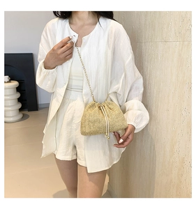 Detail of woven straw bucket bag with white drawstring closure and gold metal chain strap