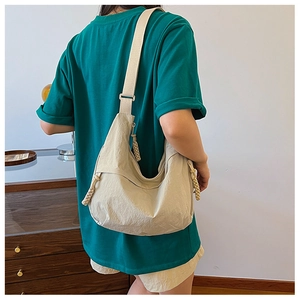 Detail of beige hobo crossbody bag with woven knot zipper on model in casual setting