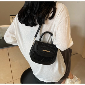 Detail of black saddle bag with textured flap and gold hardware on model's side