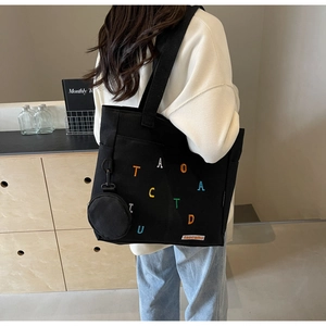 Detail of black canvas tote bag with colorful embroidery and matching mini pouch