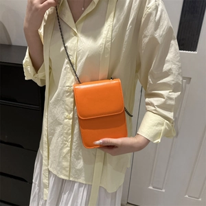 Petit sac bandoulière en similicuir orange avec fine chaîne noire porté par mannequin