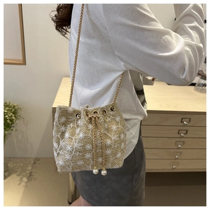 Detail of beige embroidered bucket bag with floral patterns, pearl drawstring, and gold chain
