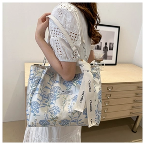 Detail of floral tote bag featuring a leather-chain strap and decorative logo ribbons