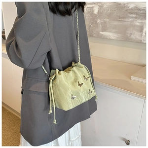 Detalle del bolso tipo saco verde menta con cordón y elegantes accesorios de mariposa plata