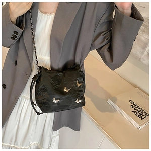 Bolso bandolera negro efecto arrugado con mariposas doradas sobre un traje gris